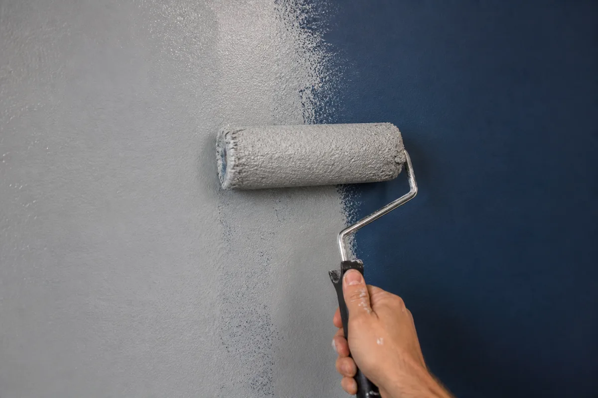 Rouleau appliquant une sous-couche grise sur un mur bleu foncé, démarcation nette entre la zone traitée et le mur d’origine
